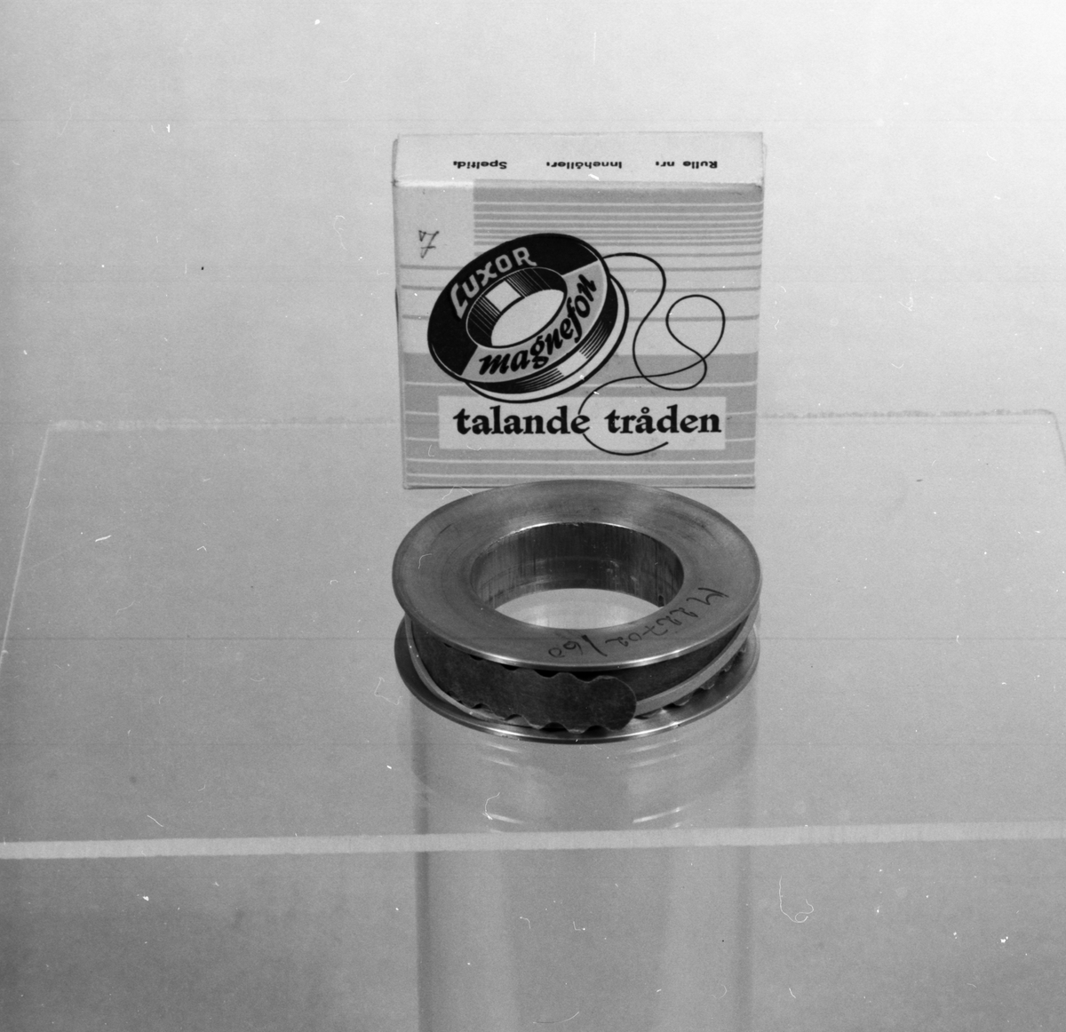 Tontråd till trådspelare, på svarvad metallspole utan etikett, märkt M 22702/60. I pappask med texten: "Luxor Magnefon, talande tråden". På medföljande pappersremsa anges: "Per Lindfors program". Spole: ytterdiameter: 70, håldiameter: 40, tjocklek: 17 mm. Kartongens längd: 80 mm, bredd: 80 mm, höjd: 20 mm.