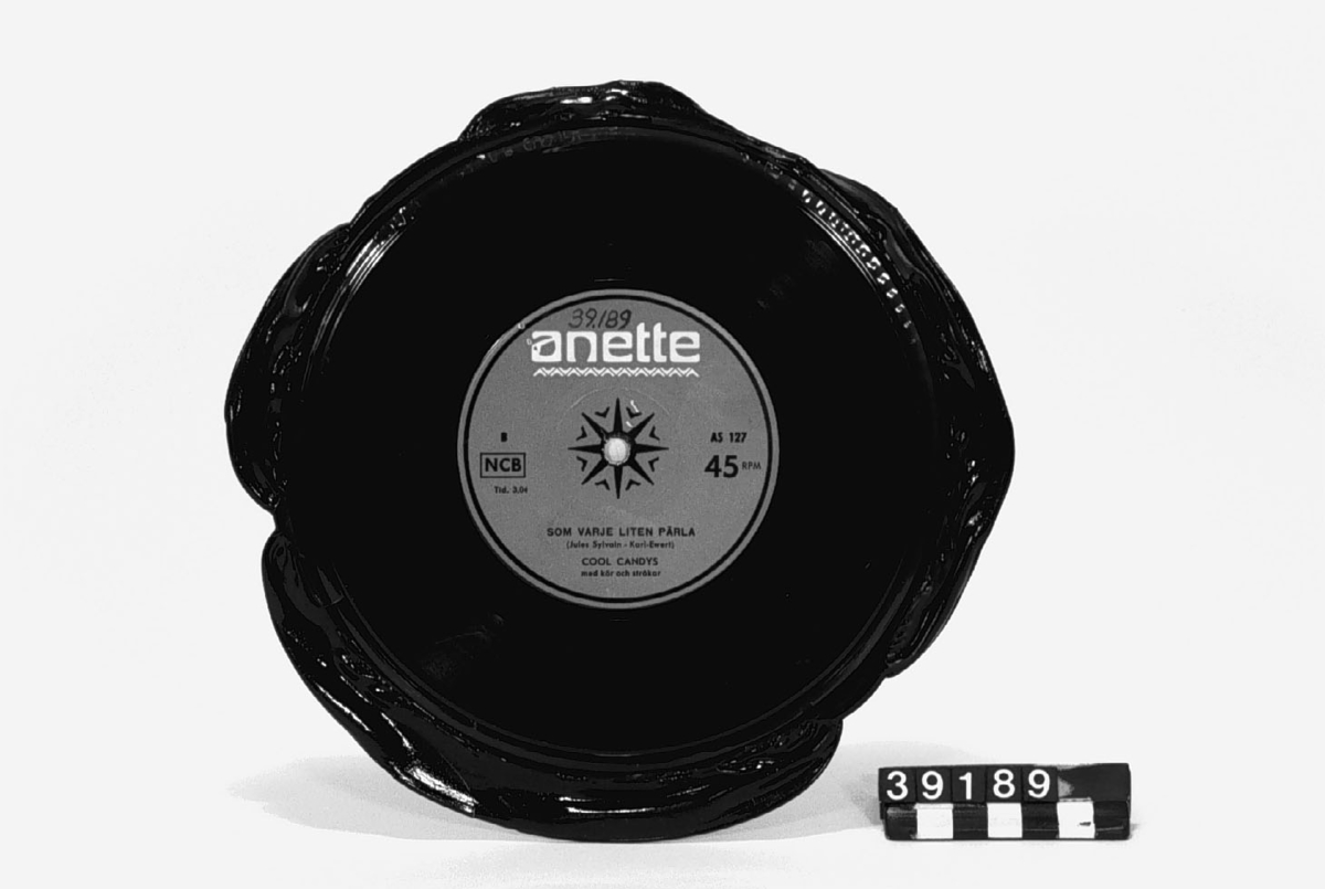 Grammofonskiva, av lack. Pressad med kvarsittande "skägg". Titlar: "Vad kärleken begär" "Som varje liten pärla". Artister: Cool Candys. Märke: Anette, röd etikett AS 127 45 RPM NCB.