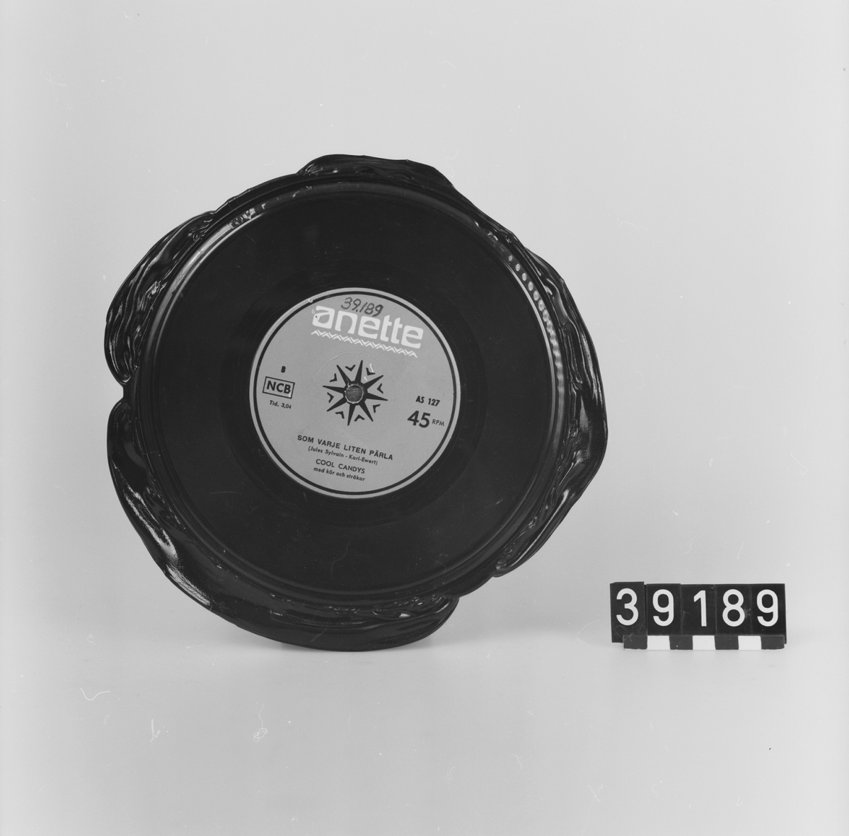 Grammofonskiva, av lack. Pressad med kvarsittande "skägg". Titlar: "Vad kärleken begär" "Som varje liten pärla". Artister: Cool Candys. Märke: Anette, röd etikett AS 127 45 RPM NCB.