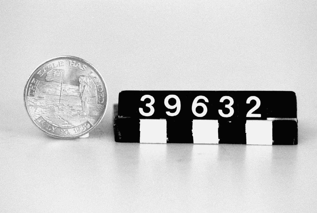 Åtsidan: Astronaut vid amerikanska flaggan vid den första månlandningen, text runtom: "The Eagle has landed July 20 1969". Baksida: "This medallion contains metal from spacecrafts Columbia and Eagle that took astronauts Armstrong Aldrin and Collins on their historic Apollo 11 mission that resulted in the first landing of man on the moon".
