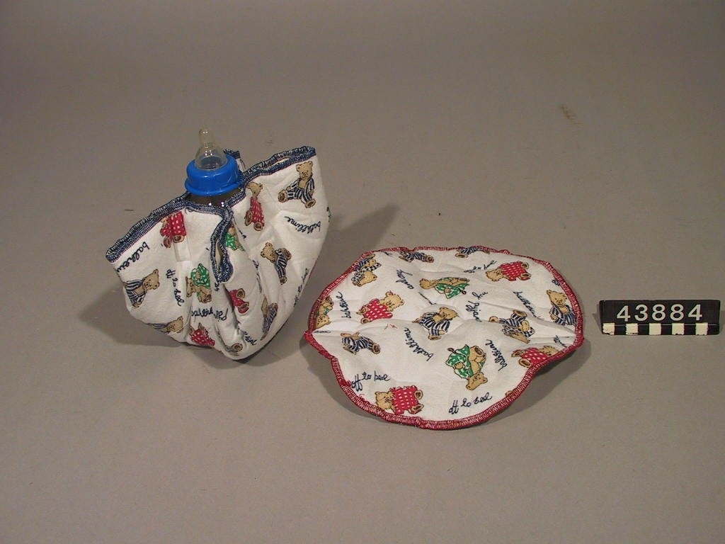 Nappflaskhölje i tyg med flera olika funktioner. Höljet bildar fyra vingar vid hopsättning. Det mjuka höljet underlättar för spädbarnet att hålla nappflaskan själv, flaskan blir mjukare och håller vällingen varm lite längre. Höljet kan också användas som en trygghetsskapande leksak.