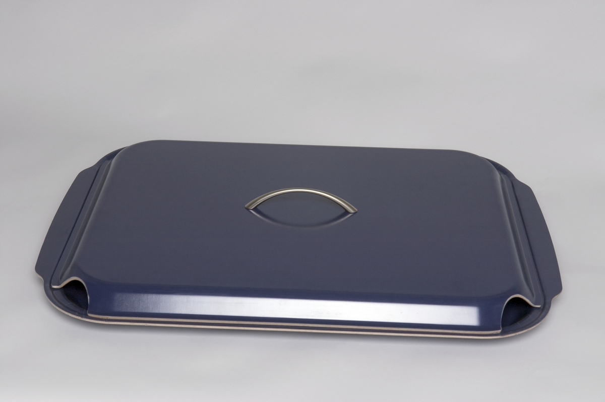 Bricka med lock. På brickan kan en hel ugnsplåt, långpanna, rymmas och serveringen direkt från långpannan kan därmed göras mer tilltalande. Locket används för att hålla maten varm, eller kall. Tillverkad av 3 mm formpressad furufanér, belagd med ett värmetåligt ytskikt av melamin.