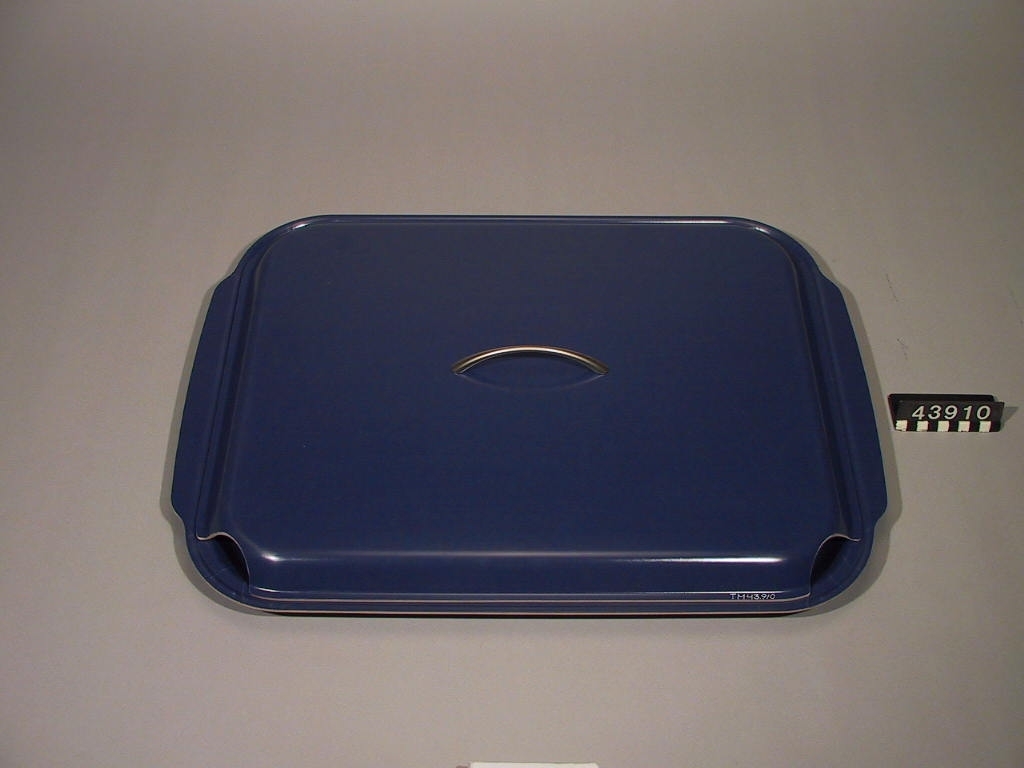 Bricka med lock. På brickan kan en hel ugnsplåt, långpanna, rymmas och serveringen direkt från långpannan kan därmed göras mer tilltalande. Locket används för att hålla maten varm, eller kall. Tillverkad av 3 mm formpressad furufanér, belagd med ett värmetåligt ytskikt av melamin.