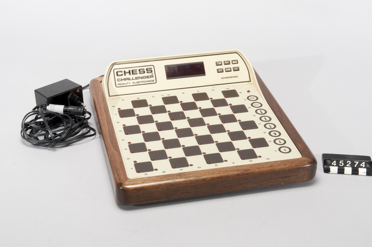 Schackautomat, Fidelity Chess Challenger Champion. Spelet ställs upp med svarta pjäser i övre ändan, mot displayen. Vid korrekt uppställning står vit kung på E1, svart på E8. Om man väljer att spela passivt ska vit kung stå på D8 och svart på D1. Genom att trycka ned spelarens kung (innan andra pjäser flyttas) går det att ställa in svårighetsgrad. Automaten registrerar sedan spelarens drag och gör egna, men spelaren måste flytta båda sidors pjäser. När automaten ställer spelaren i schack matt säger den det, också om mattdraget är oundvikligt: "Check and mate in 3".  Åtta bitars processor, MOS tech. typ 6502, 16 kB ROM, 4 kB RAM. Shackdatorn har 12 svårighetsnivåer. Den har även sensorisk röst som är datorgenererad och uttalar dragen. Det finns femtio ord i minnet, för att beskriva t ex vilken pjäs som flyttas eller om kungen står i schack. Den kan också bekräfta pjäsernas placering på brädet, på begäran av användaren.  Schackautomaten saknade vid förvärvet originalpjäserna. Patent 4.235.442