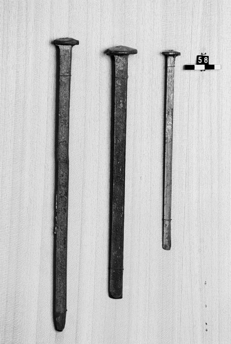 Framställda genom varmsmidning i maskin, s.k. präss-spik. Spikarna visa gränsen uppåt och nedåt (största och minsta spik) för denna tillverkning i Sverige. Mått, den större spiken: längd: 280 mm, diamanter: 28mm. Den mindre: längd: 32 mm, diameter: 6mm. Text på etikett: "Största och minsta präss-spik från Skyllberg. Present af Carl Sahlin 1922".