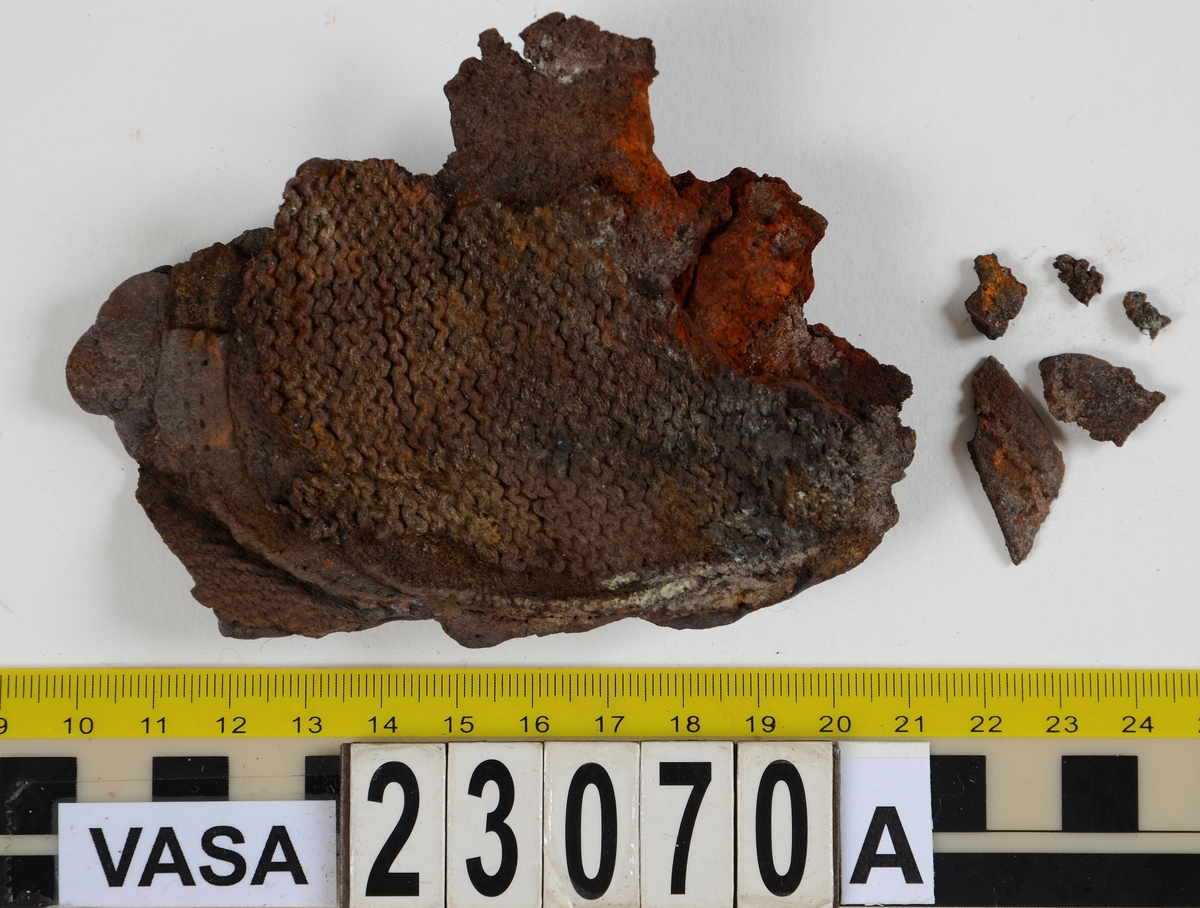 Sko.
Inuti skorna hittades även fragment från olika textilier som ursprungligen varit ett par strumpor. Idag sitter ett stickat fragment av ull fast i vänsterskon (23070) med avigsidan uppåt. I fyndet finns även en mängd lösa stickade fragment som idag är mycket korroderade och vissa helt mineraliserade av järn vilket har gjort textilen stenhård och därmed oerhört skör (23070a-c). Utifrån minskningar som några små fragment har så har det varit möjligt att rekonstruera strumpans tå. Genom att pussla ihop fragmenten som ursprungligen har suttit ihop har det på så vis gått att avgöra hur strumpans tå har varit konstruerad. Då textilen är så fragmentarisk är det inte möjligt att avgöra hur resten av strumpan har sett ut eller varit konstruerad. Däremot så finns det fragment av ett kypertvävt tyg av ull som på vissa ställen ligger dubbelt med det stickade 23070c). Ett av dessa fragment har stelnat i formen så som den suttit på fotens främre del inuti skon. Detta fragment täcker delvis det stickade tyget och har dessutom spår av kaststygn längs en kant. Så som det vävda tyget är placerat på det stickade tyget pekar på att man använt det som lagningslappar till sina stickade strumpor. 
I fyndet finns det även korroderade järnklumpar, ett tuskaftsvävt tyg av ull och rester av ett grovt bastfibergarn och två mindre läderfragment (23070d-f). Det är möjligt att även dessa har tillhört strumpan och/eller skon.

För mer detaljerad information från textildokumentationen (år 2022) se länkade filer.

Skodokumentation 2022:
Ovanläder. Tillverkad i getskinn av god kvalitet. Hör ihop med fyndnummer 23069 (Yngves skor). Tillverkades på en rak läst och bars på vänster fot. Inga dekorationer Det finns stygnhål som visar att det funnits invändiga förstärkningar (men förstärkningslappen saknas). Det finns delaminering men inga lagningar.
För mer information, se Länkade filer: Uppritning

Text in english:
This is the upper of a shoe of more “extreme fashion”, made of goatskin leather of good quality, probably made on a straight last and worn of the left foot, with no decorative features. The upper couples with 23069, together composing Yngve’s shoes. There are internal reinforcements missing from the upper and delamination, there are no repairs.
For more information, go to Länkade filer: Uppritning