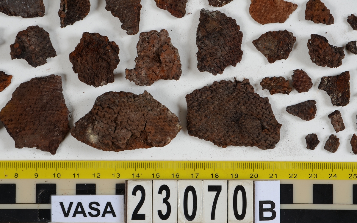 Sko.
Inuti skorna hittades även fragment från olika textilier som ursprungligen varit ett par strumpor. Idag sitter ett stickat fragment av ull fast i vänsterskon (23070) med avigsidan uppåt. I fyndet finns även en mängd lösa stickade fragment som idag är mycket korroderade och vissa helt mineraliserade av järn vilket har gjort textilen stenhård och därmed oerhört skör (23070a-c). Utifrån minskningar som några små fragment har så har det varit möjligt att rekonstruera strumpans tå. Genom att pussla ihop fragmenten som ursprungligen har suttit ihop har det på så vis gått att avgöra hur strumpans tå har varit konstruerad. Då textilen är så fragmentarisk är det inte möjligt att avgöra hur resten av strumpan har sett ut eller varit konstruerad. Däremot så finns det fragment av ett kypertvävt tyg av ull som på vissa ställen ligger dubbelt med det stickade 23070c). Ett av dessa fragment har stelnat i formen så som den suttit på fotens främre del inuti skon. Detta fragment täcker delvis det stickade tyget och har dessutom spår av kaststygn längs en kant. Så som det vävda tyget är placerat på det stickade tyget pekar på att man använt det som lagningslappar till sina stickade strumpor. 
I fyndet finns det även korroderade järnklumpar, ett tuskaftsvävt tyg av ull och rester av ett grovt bastfibergarn och två mindre läderfragment (23070d-f). Det är möjligt att även dessa har tillhört strumpan och/eller skon.

För mer detaljerad information från textildokumentationen (år 2022) se länkade filer.

Skodokumentation 2022:
Ovanläder. Tillverkad i getskinn av god kvalitet. Hör ihop med fyndnummer 23069 (Yngves skor). Tillverkades på en rak läst och bars på vänster fot. Inga dekorationer Det finns stygnhål som visar att det funnits invändiga förstärkningar (men förstärkningslappen saknas). Det finns delaminering men inga lagningar.
För mer information, se Länkade filer: Uppritning

Text in english:
This is the upper of a shoe of more “extreme fashion”, made of goatskin leather of good quality, probably made on a straight last and worn of the left foot, with no decorative features. The upper couples with 23069, together composing Yngve’s shoes. There are internal reinforcements missing from the upper and delamination, there are no repairs.
For more information, go to Länkade filer: Uppritning