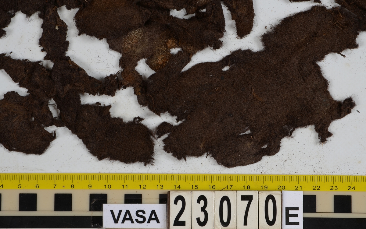 Sko.
Inuti skorna hittades även fragment från olika textilier som ursprungligen varit ett par strumpor. Idag sitter ett stickat fragment av ull fast i vänsterskon (23070) med avigsidan uppåt. I fyndet finns även en mängd lösa stickade fragment som idag är mycket korroderade och vissa helt mineraliserade av järn vilket har gjort textilen stenhård och därmed oerhört skör (23070a-c). Utifrån minskningar som några små fragment har så har det varit möjligt att rekonstruera strumpans tå. Genom att pussla ihop fragmenten som ursprungligen har suttit ihop har det på så vis gått att avgöra hur strumpans tå har varit konstruerad. Då textilen är så fragmentarisk är det inte möjligt att avgöra hur resten av strumpan har sett ut eller varit konstruerad. Däremot så finns det fragment av ett kypertvävt tyg av ull som på vissa ställen ligger dubbelt med det stickade 23070c). Ett av dessa fragment har stelnat i formen så som den suttit på fotens främre del inuti skon. Detta fragment täcker delvis det stickade tyget och har dessutom spår av kaststygn längs en kant. Så som det vävda tyget är placerat på det stickade tyget pekar på att man använt det som lagningslappar till sina stickade strumpor. 
I fyndet finns det även korroderade järnklumpar, ett tuskaftsvävt tyg av ull och rester av ett grovt bastfibergarn och två mindre läderfragment (23070d-f). Det är möjligt att även dessa har tillhört strumpan och/eller skon.

För mer detaljerad information från textildokumentationen (år 2022) se länkade filer.

Skodokumentation 2022:
Ovanläder. Tillverkad i getskinn av god kvalitet. Hör ihop med fyndnummer 23069 (Yngves skor). Tillverkades på en rak läst och bars på vänster fot. Inga dekorationer Det finns stygnhål som visar att det funnits invändiga förstärkningar (men förstärkningslappen saknas). Det finns delaminering men inga lagningar.
För mer information, se Länkade filer: Uppritning

Text in english:
This is the upper of a shoe of more “extreme fashion”, made of goatskin leather of good quality, probably made on a straight last and worn of the left foot, with no decorative features. The upper couples with 23069, together composing Yngve’s shoes. There are internal reinforcements missing from the upper and delamination, there are no repairs.
For more information, go to Länkade filer: Uppritning