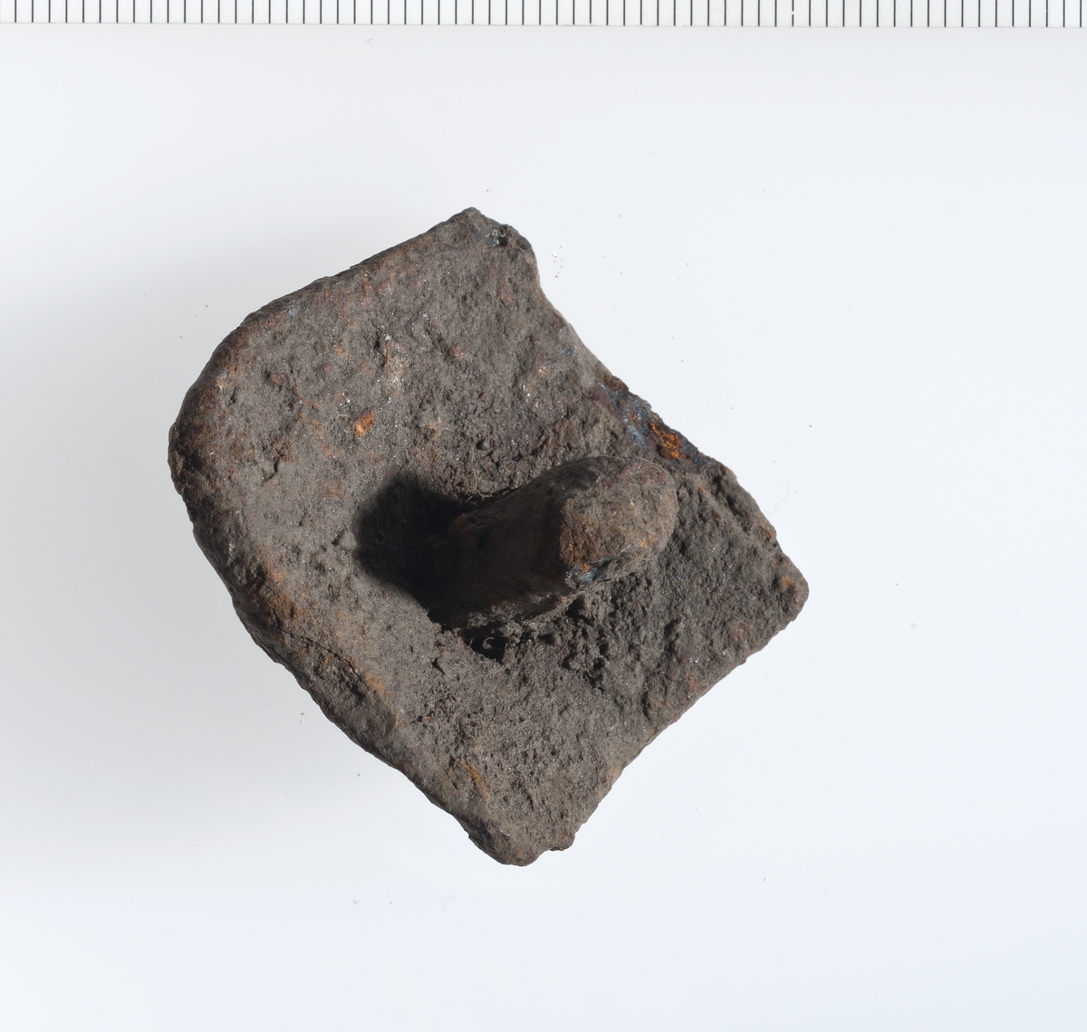 Kvadratisk metallplate med en større nagle slått gjennom i midten. Relativt rustet. 
