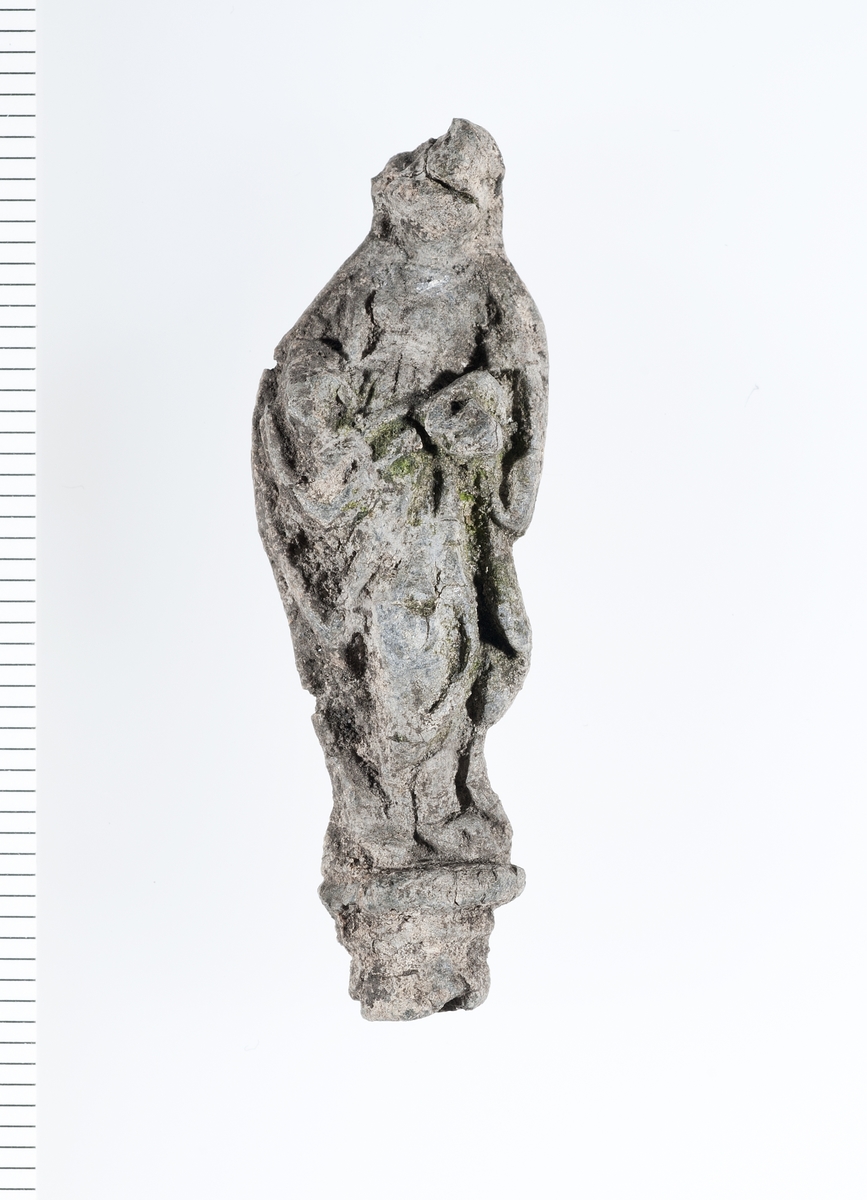 Forseggjort helfigur av en stående madonna som holder noe i armene. Motivet er noe slitt men fine detaljer i hår og klesdrakt er fortsatt tydelige. 