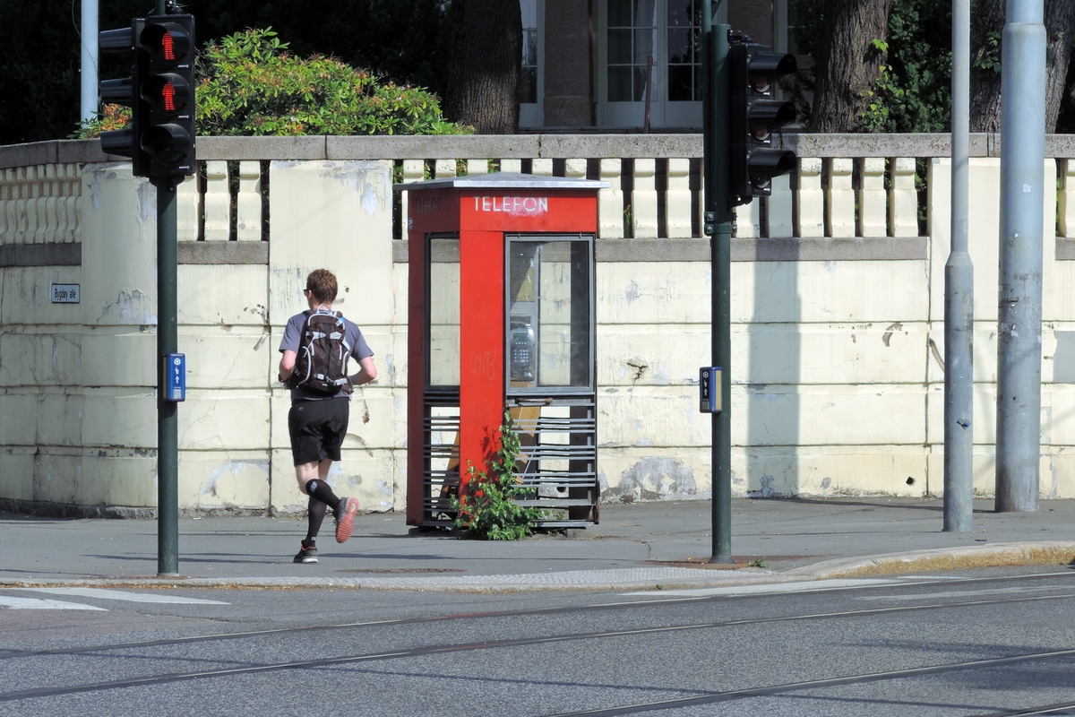 This is the story of how Norway’s most important conversation-space was designed by a young, freshly graduated man from Bergen.

“Norwegian architects are hereby invited…”
In the autumn of 1932, Oslo Telefonanlegginitiated an architectural competition. Finally, Oslo would get its own telephone booth. The city had had so called “talking-stations” from 1885, which in turn were overtaken by automatic telephones 
 only available at selected Narvesen kiosks. The state 
was of the opinion that now was the time to offer the public a better service; public telephone booths open 24/7, like the ones they already had in Sweden and England. But what would they look like, these new telephone booths? What considerations would it
 be necessary to take when designing it? The telegraph board developed a detailed list of demands and restraints: “The booth is intended to be placed outside on the streets and squares and need to be designed so that snow and ice does not hinder the opening and closing of the doors,” they wrote. “To prevent vandalism, theft, uncleanliness etc. inside the booth, it needs to be designed so that from all angles one may see what is going on in there.” Additionally, it would need to withstand storms and bad weather, and “preferably also being whipped by rain mixed with seawater” 

This was not all: The appearance would have to be «pleasing». The booth also needed to be movable, so that it could be taken in to be serviced at Telegrafverket’s main workshops. The reqired material was iron, and the surface was to be spray painted  preferably using car-body paint. There was a requirement for “a writing shelf, a pack shelf, and a suitable place for the telephone catalogue.” Also, there would need to be an illuminated TELEFON  sign, easily visible from all four angles. The total cost for each booth should not exceed 1000 kroner. The first prize for coming up with such a product was 800 kroner.

“Norwegianarchitects are hereby invited to partake in a competition for the design of a telephone booth…”  

The man with the solution
«At some point in 1932, Georg Fredrik sat at a party in Bergen. Maybe he felt a bit lost and forgotten as he often had throughout his life. He retreated to a quiet corner, took out a pencil and strted doodling on a matchbox.  According to my mother, this was how the telephone booth came into being.” In the book “Norges lille røde  historien om telefonkiosken,” Lars Fasting describes his father, the man who is far less known than the iconic architctural structure he left behind. Georg Fredrik Fasting was from Bergen, born into a family of working people and smallholders. One unusual facet of Georg Fredrik was that he was born without ears. His mother made sure he learnt to speak, read and write, 
ut Lars Fasting indicates that his father would seek refuge in drawing when the social challenges became too much to bear. And in the end drawing became his profession. In 1924 he secured a guarantor for a student loan, and started studying to become an a
rchitect at the NTH. Throughout the 1930s he entered several architectural competitions, with drafts produced, according to his son, “after work and in the late hours of the night.”

His efforts were not wasted. Out of 93 entries, with names such as “Flirt”, “Brrr”, “Ring” and “Amor”, the jury selected Fasting’s submission, “RIKS” as the new telephone booth: “The draft shows a strikingly simple solution to the task, technically as well as aesthetically well worked out.”

Taut and provident
Simple and aesthetc are the keywords here. Fasting had designed a booth pointing towards the future, and to modernism. Just how modern it was can be seen by comparing RIKS to the British telephone booth, also designed in the interwar-era. While the British version with it classicistic style is looking back to the heyday of the empire, Fasting’s booth is progressive and functionalistic. Like most Norwegian architects, Fasting broke with the classicistic style of architecture after the Stockholm-exhibition in 1930. “After it, almost all buildings erected in Norway until the German invasion in 1940, were in the functionalistic architectural style,” writes senior curator of architecture at the Norwegian National Museum, Ulf Grønvold, in the book, “Den lille røde”.“TheNorwegian booth is a piece of functionalistic architecture, an asymmetric composition with its roof slab overhanging the word TELEFON, in bold sans seraph lettering,”concludes Ulf Grønvold.

Fashionably red
And it was red. Fasting chose a colour which was part of the modern palette. “A bright red colour, but not as shiny as a signal red, the character of the colour places it among the fashionable colours within functionalism,” states paintings conservator and researcher in NIKU (Norwegian Institute for Cultural Heitage Research), Jon Brænne. In his opinion, Fasting went for visibility without making the booth stand out too much from its surroundings. The original colour was in use up to around 1950, when it changed to signal red. Towards the end of the 1970s the clour was again adjusted towards today’s orangey red.

The design, however, has not changed. RIKS is eighty years and still looks remarkably good. That’s what makes Fasting’s telephone booth a classic  even before it was added to DOCOMOMO’s list over moden icons of design. For Telenor, the telephone booth has served as a pathway into the hearts of the public. For many, Telenor (Televerket) was synonymous with exactly this telephone booth, because this was where one would go to place a call. Having a home
phone was not common until the 1980s. As such the red box became part of the Norwegian everyday and consciousness. The symbol- and publicity value of this is hard to evaluate, but in 2007 it was time to give honour where honour was due, Telenor, in consul
tation with the Directorate for Cultural Heritage, decided to preserve 100 telephone booths for all eternity.

And what about Georg Fredrik Fasting? What happened to him? At the age of 56 an entry in his diary states: «I CAN HEAR». As the first person in th world he had undergone an operation where he had ear canals constructed and eardrums fitted. For the rest of his life, the man behind Norway’s own telephone booth could answer the telephone himself.

Source: Norges lille røde historien om telefonkiosken (2007), issued by The Norwegian Telecom Museum and Telenor Cultural Heritage.
