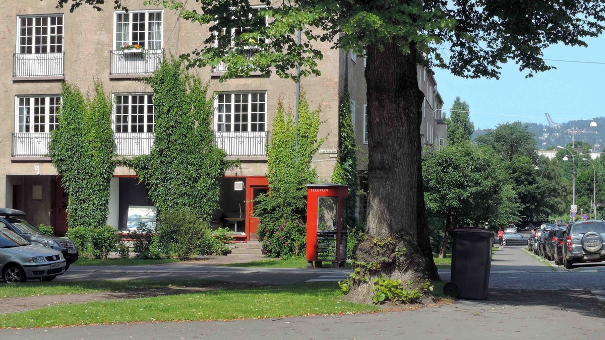 This is the story of how Norway’s most important conversation-space was designed by a young, freshly graduated man from Bergen.

“Norwegian architects are hereby invited…”
In the autumn of 1932, Oslo Telefonanlegginitiated an architectural competition. Finally, Oslo would get its own telephone booth. The city had had so called “talking-stations” from 1885, which in turn were overtaken by automatic telephones 
 only available at selected Narvesen kiosks. The state 
was of the opinion that now was the time to offer the public a better service; public telephone booths open 24/7, like the ones they already had in Sweden and England. But what would they look like, these new telephone booths? What considerations would it
 be necessary to take when designing it? The telegraph board developed a detailed list of demands and restraints: “The booth is intended to be placed outside on the streets and squares and need to be designed so that snow and ice does not hinder the opening and closing of the doors,” they wrote. “To prevent vandalism, theft, uncleanliness etc. inside the booth, it needs to be designed so that from all angles one may see what is going on in there.” Additionally, it would need to withstand storms and bad weather, and “preferably also being whipped by rain mixed with seawater” 

This was not all: The appearance would have to be «pleasing». The booth also needed to be movable, so that it could be taken in to be serviced at Telegrafverket’s main workshops. The reqired material was iron, and the surface was to be spray painted  preferably using car-body paint. There was a requirement for “a writing shelf, a pack shelf, and a suitable place for the telephone catalogue.” Also, there would need to be an illuminated TELEFON  sign, easily visible from all four angles. The total cost for each booth should not exceed 1000 kroner. The first prize for coming up with such a product was 800 kroner.

“Norwegianarchitects are hereby invited to partake in a competition for the design of a telephone booth…”  

The man with the solution
«At some point in 1932, Georg Fredrik sat at a party in Bergen. Maybe he felt a bit lost and forgotten as he often had throughout his life. He retreated to a quiet corner, took out a pencil and strted doodling on a matchbox.  According to my mother, this was how the telephone booth came into being.” In the book “Norges lille røde  historien om telefonkiosken,” Lars Fasting describes his father, the man who is far less known than the iconic architctural structure he left behind. Georg Fredrik Fasting was from Bergen, born into a family of working people and smallholders. One unusual facet of Georg Fredrik was that he was born without ears. His mother made sure he learnt to speak, read and write, 
ut Lars Fasting indicates that his father would seek refuge in drawing when the social challenges became too much to bear. And in the end drawing became his profession. In 1924 he secured a guarantor for a student loan, and started studying to become an a
rchitect at the NTH. Throughout the 1930s he entered several architectural competitions, with drafts produced, according to his son, “after work and in the late hours of the night.”

His efforts were not wasted. Out of 93 entries, with names such as “Flirt”, “Brrr”, “Ring” and “Amor”, the jury selected Fasting’s submission, “RIKS” as the new telephone booth: “The draft shows a strikingly simple solution to the task, technically as well as aesthetically well worked out.”

Taut and provident
Simple and aesthetc are the keywords here. Fasting had designed a booth pointing towards the future, and to modernism. Just how modern it was can be seen by comparing RIKS to the British telephone booth, also designed in the interwar-era. While the British version with it classicistic style is looking back to the heyday of the empire, Fasting’s booth is progressive and functionalistic. Like most Norwegian architects, Fasting broke with the classicistic style of architecture after the Stockholm-exhibition in 1930. “After it, almost all buildings erected in Norway until the German invasion in 1940, were in the functionalistic architectural style,” writes senior curator of architecture at the Norwegian National Museum, Ulf Grønvold, in the book, “Den lille røde”.“TheNorwegian booth is a piece of functionalistic architecture, an asymmetric composition with its roof slab overhanging the word TELEFON, in bold sans seraph lettering,”concludes Ulf Grønvold.

Fashionably red
And it was red. Fasting chose a colour which was part of the modern palette. “A bright red colour, but not as shiny as a signal red, the character of the colour places it among the fashionable colours within functionalism,” states paintings conservator and researcher in NIKU (Norwegian Institute for Cultural Heitage Research), Jon Brænne. In his opinion, Fasting went for visibility without making the booth stand out too much from its surroundings. The original colour was in use up to around 1950, when it changed to signal red. Towards the end of the 1970s the clour was again adjusted towards today’s orangey red.

The design, however, has not changed. RIKS is eighty years and still looks remarkably good. That’s what makes Fasting’s telephone booth a classic  even before it was added to DOCOMOMO’s list over moden icons of design. For Telenor, the telephone booth has served as a pathway into the hearts of the public. For many, Telenor (Televerket) was synonymous with exactly this telephone booth, because this was where one would go to place a call. Having a home
phone was not common until the 1980s. As such the red box became part of the Norwegian everyday and consciousness. The symbol- and publicity value of this is hard to evaluate, but in 2007 it was time to give honour where honour was due, Telenor, in consul
tation with the Directorate for Cultural Heritage, decided to preserve 100 telephone booths for all eternity.

And what about Georg Fredrik Fasting? What happened to him? At the age of 56 an entry in his diary states: «I CAN HEAR». As the first person in th world he had undergone an operation where he had ear canals constructed and eardrums fitted. For the rest of his life, the man behind Norway’s own telephone booth could answer the telephone himself.

Source: Norges lille røde historien om telefonkiosken (2007), issued by The Norwegian Telecom Museum and Telenor Cultural Heritage.