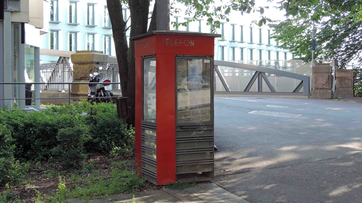 This is the story of how Norway’s most important conversation-space was designed by a young, freshly graduated man from Bergen.

“Norwegian architects are hereby invited…”
In the autumn of 1932, Oslo Telefonanlegginitiated an architectural competition. Finally, Oslo would get its own telephone booth. The city had had so called “talking-stations” from 1885, which in turn were overtaken by automatic telephones 
 only available at selected Narvesen kiosks. The state 
was of the opinion that now was the time to offer the public a better service; public telephone booths open 24/7, like the ones they already had in Sweden and England. But what would they look like, these new telephone booths? What considerations would it
 be necessary to take when designing it? The telegraph board developed a detailed list of demands and restraints: “The booth is intended to be placed outside on the streets and squares and need to be designed so that snow and ice does not hinder the opening and closing of the doors,” they wrote. “To prevent vandalism, theft, uncleanliness etc. inside the booth, it needs to be designed so that from all angles one may see what is going on in there.” Additionally, it would need to withstand storms and bad weather, and “preferably also being whipped by rain mixed with seawater” 

This was not all: The appearance would have to be «pleasing». The booth also needed to be movable, so that it could be taken in to be serviced at Telegrafverket’s main workshops. The reqired material was iron, and the surface was to be spray painted  preferably using car-body paint. There was a requirement for “a writing shelf, a pack shelf, and a suitable place for the telephone catalogue.” Also, there would need to be an illuminated TELEFON  sign, easily visible from all four angles. The total cost for each booth should not exceed 1000 kroner. The first prize for coming up with such a product was 800 kroner.

“Norwegianarchitects are hereby invited to partake in a competition for the design of a telephone booth…”  

The man with the solution
«At some point in 1932, Georg Fredrik sat at a party in Bergen. Maybe he felt a bit lost and forgotten as he often had throughout his life. He retreated to a quiet corner, took out a pencil and strted doodling on a matchbox.  According to my mother, this was how the telephone booth came into being.” In the book “Norges lille røde  historien om telefonkiosken,” Lars Fasting describes his father, the man who is far less known than the iconic architctural structure he left behind. Georg Fredrik Fasting was from Bergen, born into a family of working people and smallholders. One unusual facet of Georg Fredrik was that he was born without ears. His mother made sure he learnt to speak, read and write, 
ut Lars Fasting indicates that his father would seek refuge in drawing when the social challenges became too much to bear. And in the end drawing became his profession. In 1924 he secured a guarantor for a student loan, and started studying to become an a
rchitect at the NTH. Throughout the 1930s he entered several architectural competitions, with drafts produced, according to his son, “after work and in the late hours of the night.”

His efforts were not wasted. Out of 93 entries, with names such as “Flirt”, “Brrr”, “Ring” and “Amor”, the jury selected Fasting’s submission, “RIKS” as the new telephone booth: “The draft shows a strikingly simple solution to the task, technically as well as aesthetically well worked out.”

Taut and provident
Simple and aesthetc are the keywords here. Fasting had designed a booth pointing towards the future, and to modernism. Just how modern it was can be seen by comparing RIKS to the British telephone booth, also designed in the interwar-era. While the British version with it classicistic style is looking back to the heyday of the empire, Fasting’s booth is progressive and functionalistic. Like most Norwegian architects, Fasting broke with the classicistic style of architecture after the Stockholm-exhibition in 1930. “After it, almost all buildings erected in Norway until the German invasion in 1940, were in the functionalistic architectural style,” writes senior curator of architecture at the Norwegian National Museum, Ulf Grønvold, in the book, “Den lille røde”.“TheNorwegian booth is a piece of functionalistic architecture, an asymmetric composition with its roof slab overhanging the word TELEFON, in bold sans seraph lettering,”concludes Ulf Grønvold.

Fashionably red
And it was red. Fasting chose a colour which was part of the modern palette. “A bright red colour, but not as shiny as a signal red, the character of the colour places it among the fashionable colours within functionalism,” states paintings conservator and researcher in NIKU (Norwegian Institute for Cultural Heitage Research), Jon Brænne. In his opinion, Fasting went for visibility without making the booth stand out too much from its surroundings. The original colour was in use up to around 1950, when it changed to signal red. Towards the end of the 1970s the clour was again adjusted towards today’s orangey red.

The design, however, has not changed. RIKS is eighty years and still looks remarkably good. That’s what makes Fasting’s telephone booth a classic  even before it was added to DOCOMOMO’s list over moden icons of design. For Telenor, the telephone booth has served as a pathway into the hearts of the public. For many, Telenor (Televerket) was synonymous with exactly this telephone booth, because this was where one would go to place a call. Having a home
phone was not common until the 1980s. As such the red box became part of the Norwegian everyday and consciousness. The symbol- and publicity value of this is hard to evaluate, but in 2007 it was time to give honour where honour was due, Telenor, in consul
tation with the Directorate for Cultural Heritage, decided to preserve 100 telephone booths for all eternity.

And what about Georg Fredrik Fasting? What happened to him? At the age of 56 an entry in his diary states: «I CAN HEAR». As the first person in th world he had undergone an operation where he had ear canals constructed and eardrums fitted. For the rest of his life, the man behind Norway’s own telephone booth could answer the telephone himself.

Source: Norges lille røde historien om telefonkiosken (2007), issued by The Norwegian Telecom Museum and Telenor Cultural Heritage.