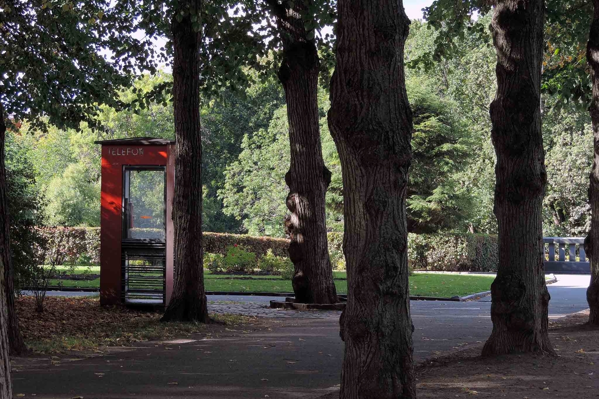 This is the story of how Norway’s most important conversation-space was designed by a young, freshly graduated man from Bergen.

“Norwegian architects are hereby invited…”
In the autumn of 1932, Oslo Telefonanlegginitiated an architectural competition. Finally, Oslo would get its own telephone booth. The city had had so called “talking-stations” from 1885, which in turn were overtaken by automatic telephones 
 only available at selected Narvesen kiosks. The state 
was of the opinion that now was the time to offer the public a better service; public telephone booths open 24/7, like the ones they already had in Sweden and England. But what would they look like, these new telephone booths? What considerations would it
 be necessary to take when designing it? The telegraph board developed a detailed list of demands and restraints: “The booth is intended to be placed outside on the streets and squares and need to be designed so that snow and ice does not hinder the opening and closing of the doors,” they wrote. “To prevent vandalism, theft, uncleanliness etc. inside the booth, it needs to be designed so that from all angles one may see what is going on in there.” Additionally, it would need to withstand storms and bad weather, and “preferably also being whipped by rain mixed with seawater” 

This was not all: The appearance would have to be «pleasing». The booth also needed to be movable, so that it could be taken in to be serviced at Telegrafverket’s main workshops. The reqired material was iron, and the surface was to be spray painted  preferably using car-body paint. There was a requirement for “a writing shelf, a pack shelf, and a suitable place for the telephone catalogue.” Also, there would need to be an illuminated TELEFON  sign, easily visible from all four angles. The total cost for each booth should not exceed 1000 kroner. The first prize for coming up with such a product was 800 kroner.

“Norwegianarchitects are hereby invited to partake in a competition for the design of a telephone booth…”  

The man with the solution
«At some point in 1932, Georg Fredrik sat at a party in Bergen. Maybe he felt a bit lost and forgotten as he often had throughout his life. He retreated to a quiet corner, took out a pencil and strted doodling on a matchbox.  According to my mother, this was how the telephone booth came into being.” In the book “Norges lille røde  historien om telefonkiosken,” Lars Fasting describes his father, the man who is far less known than the iconic architctural structure he left behind. Georg Fredrik Fasting was from Bergen, born into a family of working people and smallholders. One unusual facet of Georg Fredrik was that he was born without ears. His mother made sure he learnt to speak, read and write, 
ut Lars Fasting indicates that his father would seek refuge in drawing when the social challenges became too much to bear. And in the end drawing became his profession. In 1924 he secured a guarantor for a student loan, and started studying to become an a
rchitect at the NTH. Throughout the 1930s he entered several architectural competitions, with drafts produced, according to his son, “after work and in the late hours of the night.”

His efforts were not wasted. Out of 93 entries, with names such as “Flirt”, “Brrr”, “Ring” and “Amor”, the jury selected Fasting’s submission, “RIKS” as the new telephone booth: “The draft shows a strikingly simple solution to the task, technically as well as aesthetically well worked out.”

Taut and provident
Simple and aesthetc are the keywords here. Fasting had designed a booth pointing towards the future, and to modernism. Just how modern it was can be seen by comparing RIKS to the British telephone booth, also designed in the interwar-era. While the British version with it classicistic style is looking back to the heyday of the empire, Fasting’s booth is progressive and functionalistic. Like most Norwegian architects, Fasting broke with the classicistic style of architecture after the Stockholm-exhibition in 1930. “After it, almost all buildings erected in Norway until the German invasion in 1940, were in the functionalistic architectural style,” writes senior curator of architecture at the Norwegian National Museum, Ulf Grønvold, in the book, “Den lille røde”.“TheNorwegian booth is a piece of functionalistic architecture, an asymmetric composition with its roof slab overhanging the word TELEFON, in bold sans seraph lettering,”concludes Ulf Grønvold.

Fashionably red
And it was red. Fasting chose a colour which was part of the modern palette. “A bright red colour, but not as shiny as a signal red, the character of the colour places it among the fashionable colours within functionalism,” states paintings conservator and researcher in NIKU (Norwegian Institute for Cultural Heitage Research), Jon Brænne. In his opinion, Fasting went for visibility without making the booth stand out too much from its surroundings. The original colour was in use up to around 1950, when it changed to signal red. Towards the end of the 1970s the clour was again adjusted towards today’s orangey red.

The design, however, has not changed. RIKS is eighty years and still looks remarkably good. That’s what makes Fasting’s telephone booth a classic  even before it was added to DOCOMOMO’s list over moden icons of design. For Telenor, the telephone booth has served as a pathway into the hearts of the public. For many, Telenor (Televerket) was synonymous with exactly this telephone booth, because this was where one would go to place a call. Having a home
phone was not common until the 1980s. As such the red box became part of the Norwegian everyday and consciousness. The symbol- and publicity value of this is hard to evaluate, but in 2007 it was time to give honour where honour was due, Telenor, in consul
tation with the Directorate for Cultural Heritage, decided to preserve 100 telephone booths for all eternity.

And what about Georg Fredrik Fasting? What happened to him? At the age of 56 an entry in his diary states: «I CAN HEAR». As the first person in th world he had undergone an operation where he had ear canals constructed and eardrums fitted. For the rest of his life, the man behind Norway’s own telephone booth could answer the telephone himself.

Source: Norges lille røde historien om telefonkiosken (2007), issued by The Norwegian Telecom Museum and Telenor Cultural Heritage.