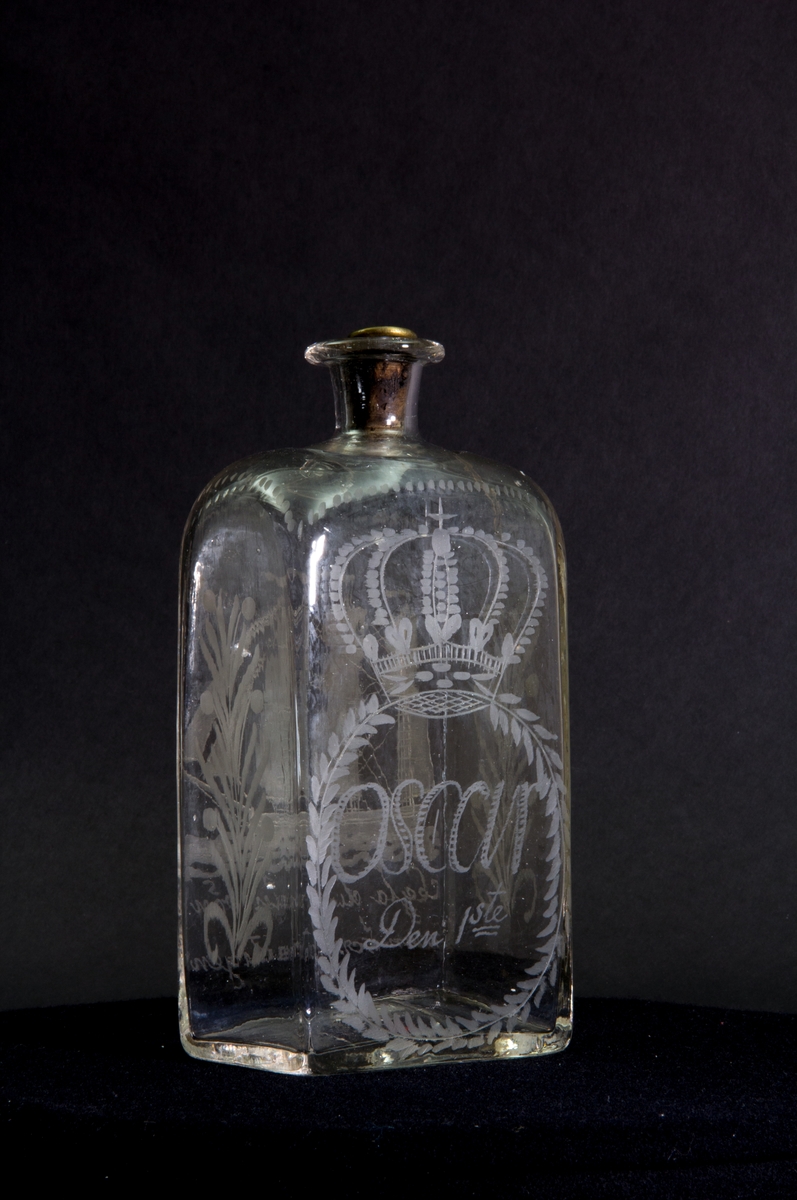 Längs flaskans övre kant en dekorativ bård av prickar. Gravyr på ena långsidan föreställande ett tremastat skepp med fulla segel. Gravyr på andra långsidan föreställande en sluten krona ovanför en lagerkrans som omsluter texten "Oscar Den 1ste". Blomstergirlanger på flaskans kortsidor.