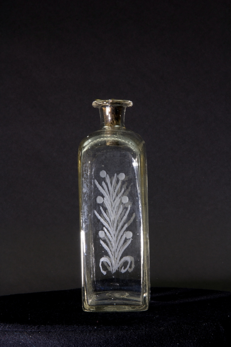 Längs flaskans övre kant en dekorativ bård av prickar. Gravyr på ena långsidan föreställande ett tremastat skepp med fulla segel. Gravyr på andra långsidan föreställande en sluten krona ovanför en lagerkrans som omsluter texten "Oscar Den 1ste". Blomstergirlanger på flaskans kortsidor.