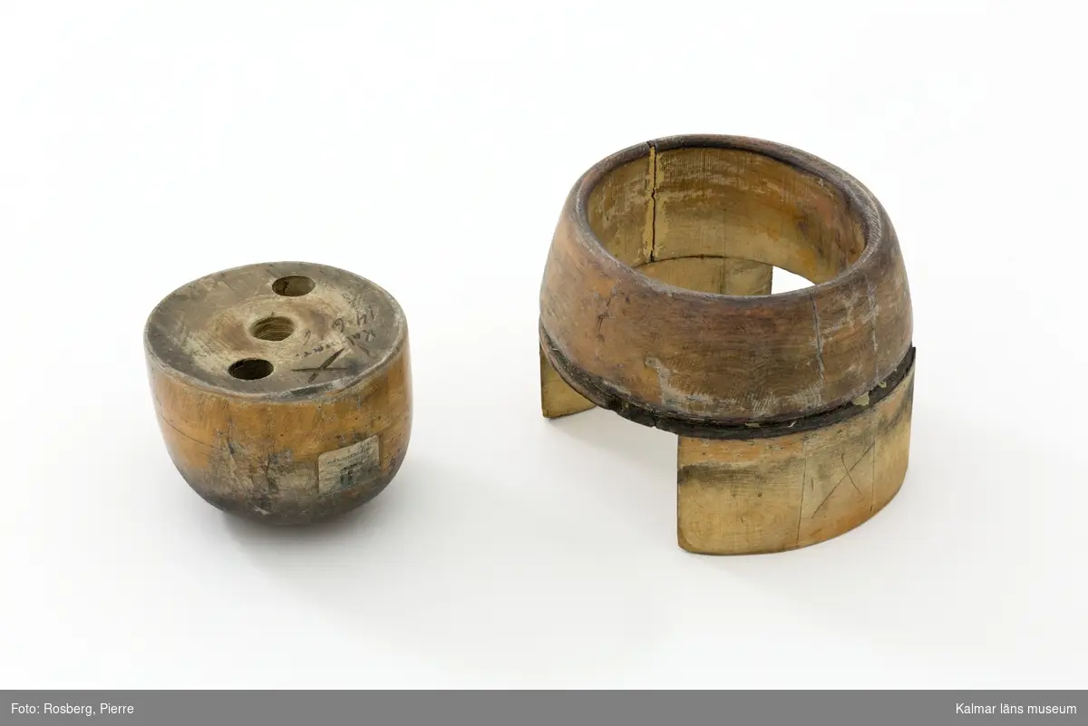 KLM 29767. Hattstock, damhattstock, kennedyhatt. Hattstock av trä med ett runt om, högt, uppvikt brätte. Slät kulle. Hattstocken består av ett brätte på två fötter och en lös kulle som placeras i brättet. På kullens undersida finns tre borrade hål, som troligtvis har använts som handtag. Intill dessa finns texten "Kalmar." och siffran 146 skrivet med svart tusch, samt ett inristat kryss. På kullens ena kortsida är även en lapp fastklistrad med texten "En produkt från HATTSTOCKSFABRIKEN GÄLLSTAD". Under hattillverkningen använde man sig av hattstockar för att få fram formen på hatten, det gjorde man genom att trä på stumpen eller kaplinen på stocken. Hattstockens form är därmed avgörande för hattens utseende. Denna modell användes vid tillverkningen av damhattar och är av form 146.