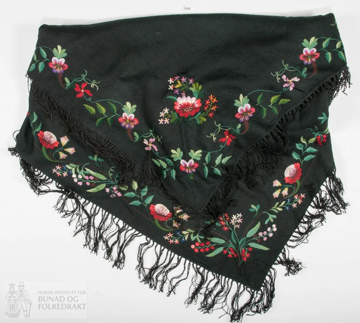 Sjal i svart ullkypert, lett valka. To høgder er sydd saman på langs, med svært tette kastesting i svart voksa tråd. Brodert i alle sider med laustvinna ullgarn i fleire fargar. Plattsaum, sjattersaum, kontursting. Brodert på retta i eine snippen og på vranga i den motståande. Frynser i svart ullgarn i tre sider, sausesvarte frynser i den siste. Sjalet er bretta og brodert slik at båe snippane skal visast.