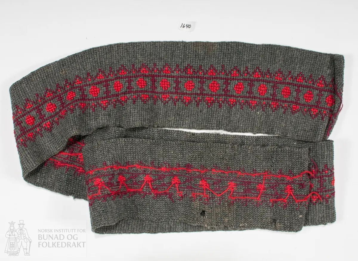 Band i grått, melert ullgarn. Truleg hakka på langs. Brodert med korssting i raudt og magentafarga ullgarn.
