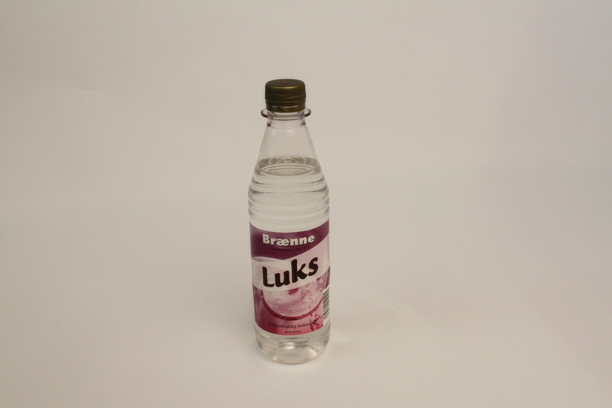 Brusflaske i gjennomsiktig plast. Etikett i rosa og lilla. Stripe på skrå over etiketten med produktnamn Luks i svart og rosa.
Motiv er prega av vatn i rørsle.