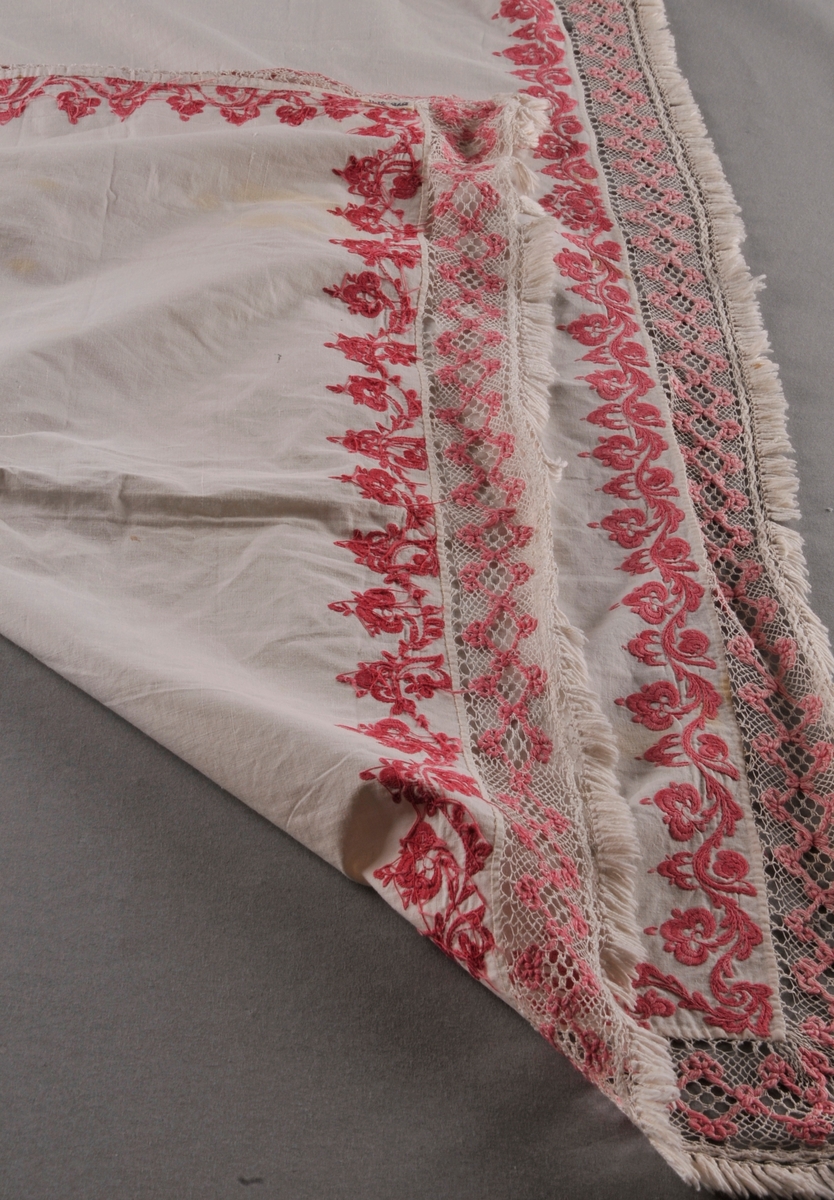 Rektangulært stykke av bomullslerret med rosa rosesaum kring alle sider. Ei påsauma kvit og rosa blonde i Telemarksbinding, i to ulike bredder, langs alle sidene.