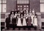 Folkskolan. Skolklass. Övre raden fr. vänster: 1. Folkskollärare Augusta Hallenius, 7. Ingeborg Johansson, 8. Harriet Fredriksson f. Bohlin. 2:a raden: 1. Ellen Jonsson, Wetterlinsgården, 4. Elsa Noring, slöjdlärare, 5. Ruth Andersson, bagare. 3:e raden: 4. Anna Eriksson (Norders Bokhandel), 5. Lilly Wennberg. 4:e raden = främre raden: 1. Märta Borg, 2. Ester Hjertman, 3. Elna Johansson, 4. Linnea Spångberg, 5. Jenny Leijon, 6. Elvira Sand.