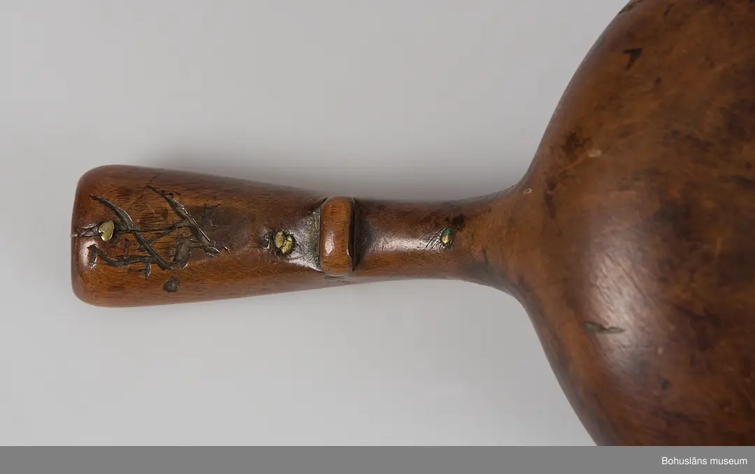 Rund skålformad kåsa med handtag skuret ur ett stycke. Mynningskanten är något indragen och mittemot handtaget är kanten upphöjd.
På utsidan kanten löper en ristad vågformad dekor.
Skaftet är böjt och bredare baktill. Ovansidan har en hornbit fastsatt med mässingsnubb. Hornbiten har ristad dekor med vågformad kant samt ett litet kors och en större korsliknande dekor.
På handtagets undersida finns ett tvärgående, utstickande parti troligtvis för att kunna hålla den lättare eller för att vila den på ett kärls kant.
Upptill på handtagets undersida finns ett inristat bomärke.
En bit av hornbiten är mörkare och sekundärt ilagad.
Kåsan har en spricka i kantens upphöjning. Inuti är det ärggröna fläckar.
Tre små hål, troligtvis efter häftstift.

Uppgifter i samband med besök från Ájtte, Svenskt Fjäll- och Samemuseum, Jokkmokk:
Lulesamisk, låg modell. Ägarnas bomärke

Ur handskrivna katalogen 1957-1958:
Träskål
Diam.: 8,5. Skopa el. Slev av trä. Föremålet helt. Lappland

Lappkatalog: 7