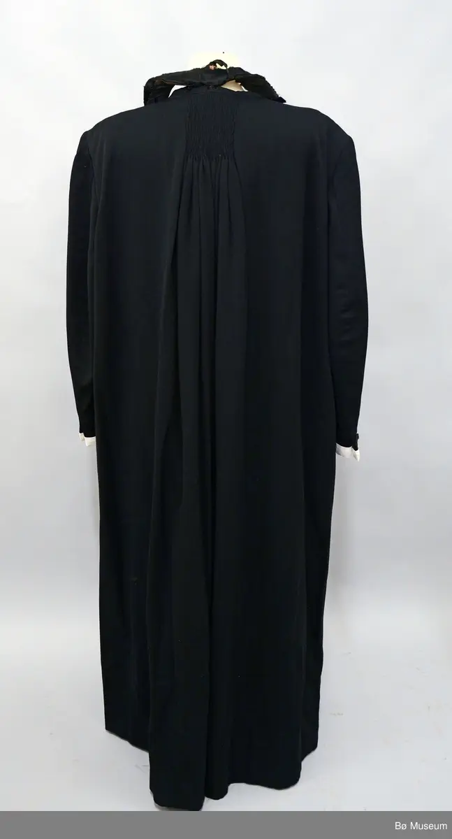 Svart fotsid samarie med tilhørende pipekrave (BØB.1995:0338.B). Drakten har langt bånd som er festet i kraven samt hvite mansjetter med hullsøm på ermene.

Fra registeringskort: Det lause bandet som går rundt nakken og ned på kvar side framme har stivt innlegg ned til liv et overtrekt med ullstoff. Frå livet og ned er fleire lag ull- stoff heile vegen overtrekt med svart sateng i ull og silke. Banda er feste med knappar til samarien, 5 på kvar side. Midt i nakken er det sydd fast til halslinninga. 21 knappar framme, trekte med silkesateng og markering av knapphol. Skjult knapping med 10 trekte knappar. Stor vidde i ryggen.