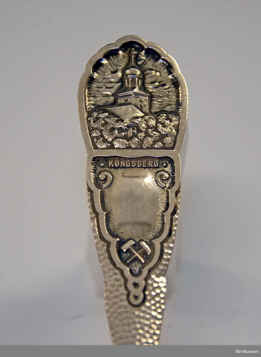 Spiseskje, sølv - med Kongsberg kirke motiv øverst på skaftet. Hører sammen med gaffel BØB.2015:0155.
 
Stempel: 830 S og J. M. JOHANSEN.
Mønster: Spesialprodusert - "KONGSBERG", to hammere (bergverksdriften) og Kongsberg kirke.