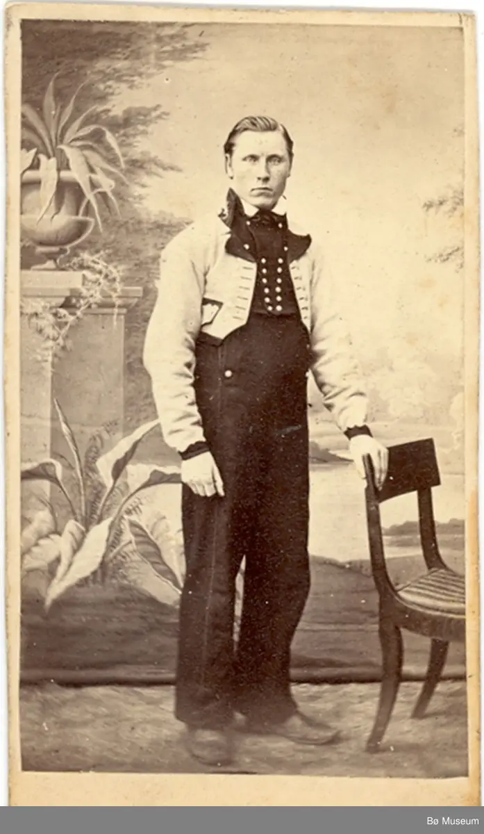 Yngre mann, fotograf Halvor H. Skogen, i gråkufte/langbukse ståande i atelier.