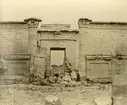 Vy över tempelområdet Medinet Habu i Thebe, Egypten. Två stående och en sittande man.

Påskrift i blyerts på baksidan möjligtvis Medinet Abou Ptoléméer porten 
Påskrift i bild A. Beato.