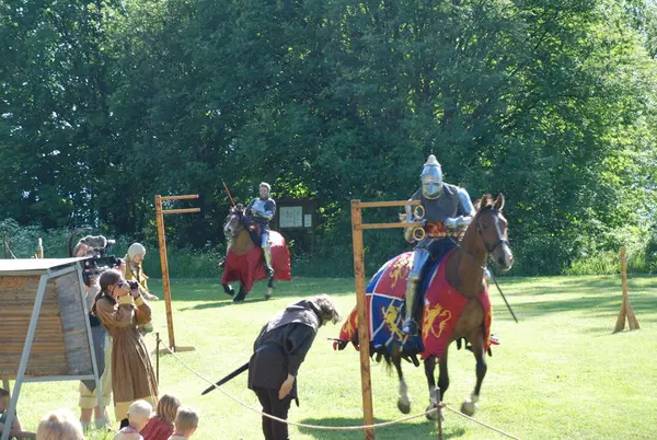 Ridder på hest i platerustning plukker ned ringer med lansen