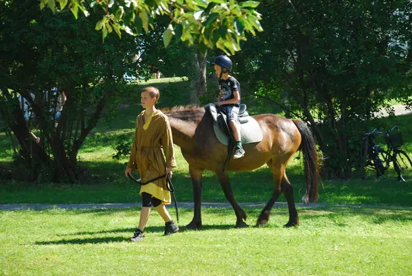 Boy on brown horse beeing led by a boy in medieval clothes