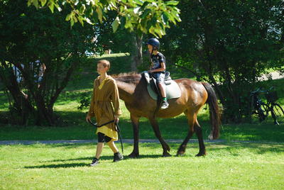 Boy on brown horse beeing led by a boy in medieval clothes