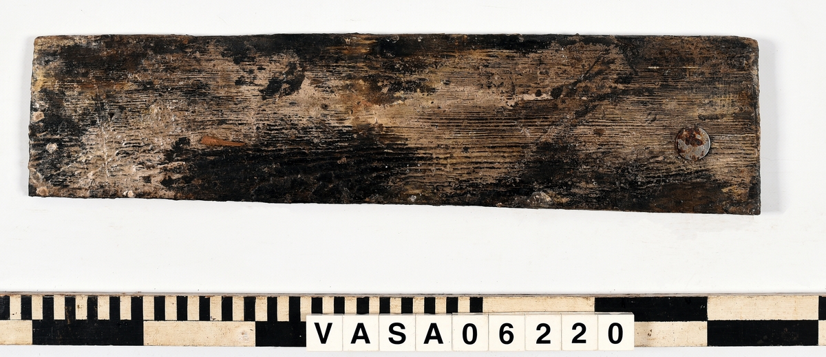 Avsmalnande bräda med två synliga spikhål. 
Lätt vittrad, tunt lager PEG.