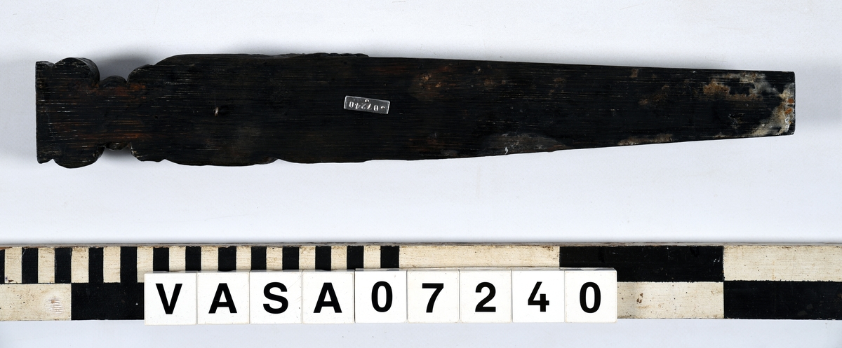 Hermpilaster.

Liten pilaster i form av en karyatid, med långt böljande hår under joniskt kapitäl.

Huvudet är vridet en aning åt höger. Med vänster hand hålls manteln samlad. I höger hand håller figuren en frukt eller dylikt framför bröstet. Pilasterskaftet är prytt med stora frukter och blad, fasthängande vid en stängel som delvis täcker det nedåt avsmalnande skaftets ramverk. Baksidan är slät.

Skulpturen är välbevarad, förutom ansiktet som är kraftigt slitet.

Fyra stycken spikhål, en övertäckt med en plugg.


Text in English: Sculpted small pilaster with a Caryatid with long wavy hair beneath an Ionic capital.

Its head is turned slightly to the right, its left hand holds its gathered mantle. Its right hand holds fruit or the like in front of its brests. The shaft of the pilaster is decorated with fruit and large leaves hanging from a stalk, which partly cover the framing of the tapering shaft. Its back is flat.

The sculpture is somewhat worn, its facial expression has been obliterated.