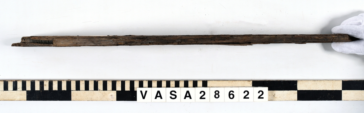 Odekorerad trapetsoid med spont på båda ändarna och sex spikhål, fem längsmed den längsta långsidan en på toppen av kortaste långsidan. Den ena sponten är helt avbruten. Torr och flagnande yta.