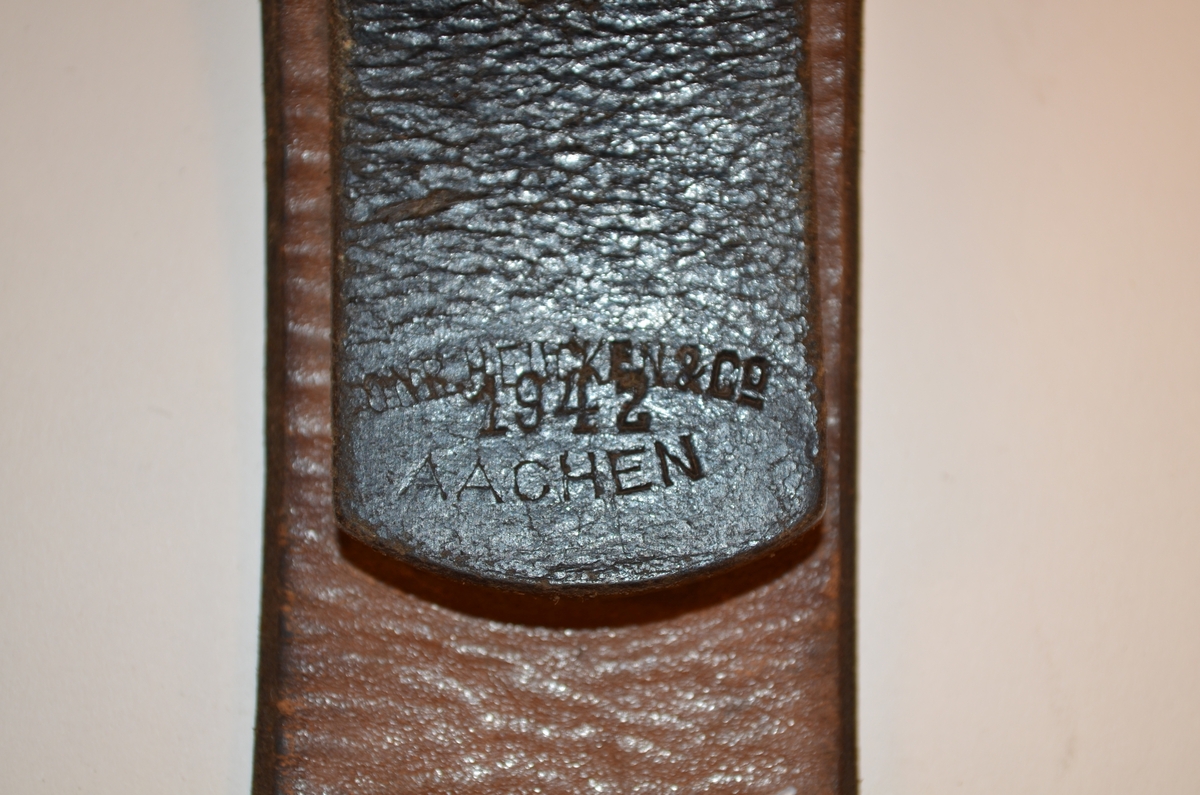Brunsvart belte tilhørende uniform brukt av den tyske okkupasjonsmakten i Norge under andre verdenskrig. Beltet er av lær med beltespenne i metall. Emblemet med den tyske ørn og hakekors er skrapet bort fra beltespennen. Stempel på innsiden av læret, hvor "Aachen 1942" kan tydes. Varemerke utydelig.