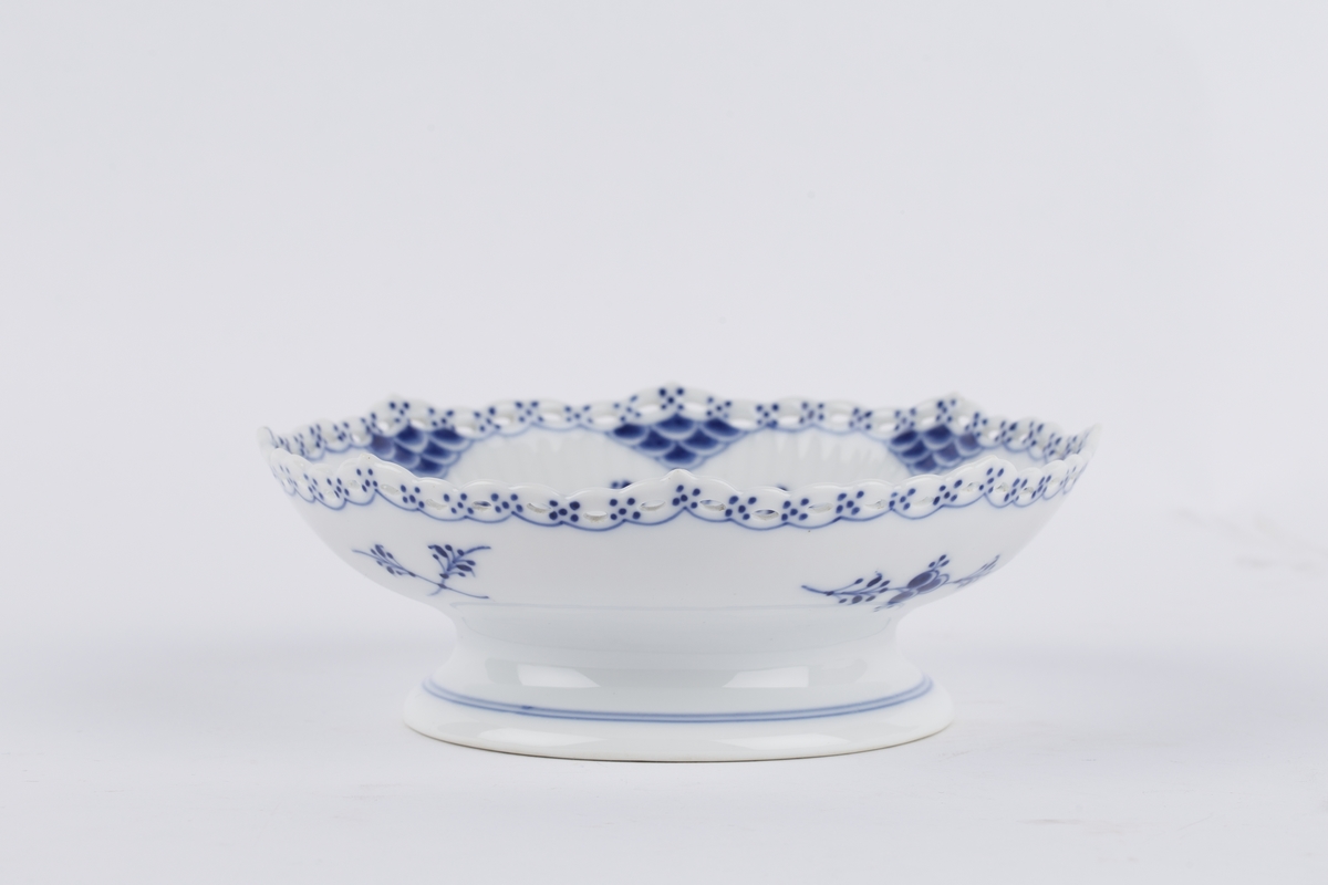 Ovalt stettfat i riflet gods med blått musselmalt mønster med gjenombrudt blondekant. Fabrikkmerket med Royal Copenhagens tre bølger samt malersignatur.