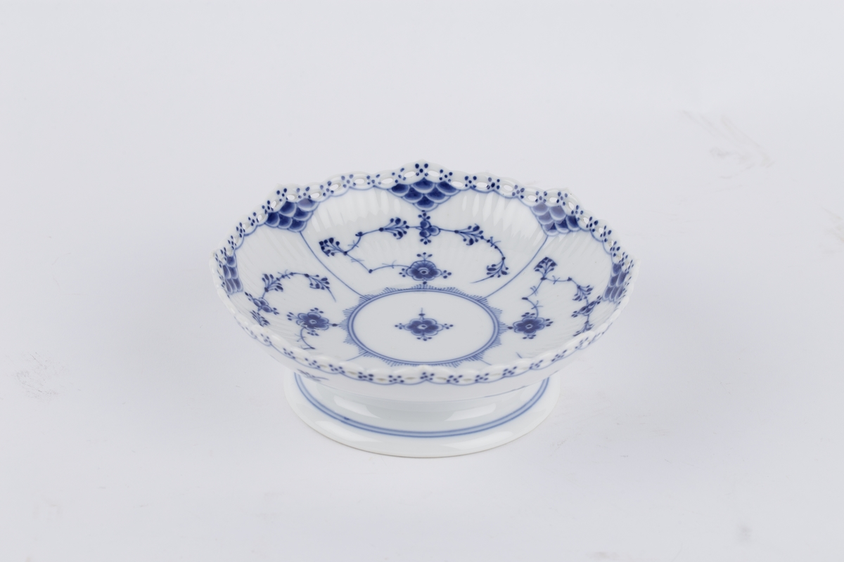 Ovalt stettfat i riflet gods med blått musselmalt mønster med gjenombrudt blondekant. Fabrikkmerket med Royal Copenhagens tre bølger samt malersignatur.