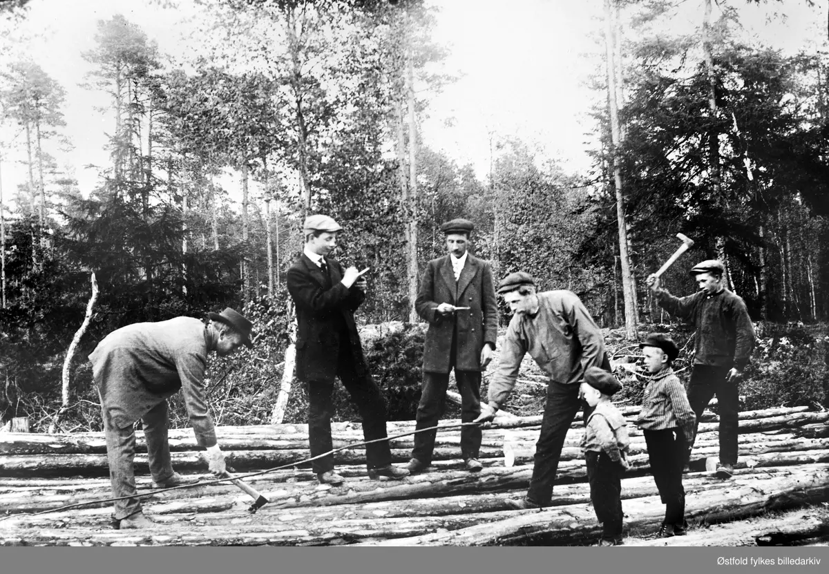 Tømmermerking i Aremark, ca. 1915. To små gutter ser på.  
Anders Tangen bøyd med øks.