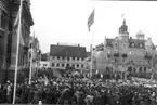 Okänd manifestation på Stortorget. Att döma av hur människorna står, med fri gång från Domkyrkans södra port, väntar man på någon procession in i eller ut ur kyrkan. Det har framförts att bilden skulle visa protestmötet mot indragningen av Kalmar stift, men då detta möte hölls 1903 borde flaggorna i så fall haft unionsmärket, d v s den norska flaggan i övre högra hörnet.