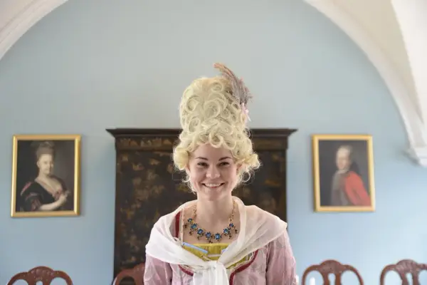 Dame sett forfra med høy parykk og fjær. Pent pyntet.