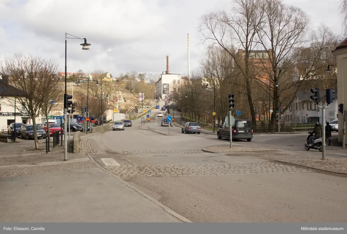 Vy från Gamla torget mot backen Kråkan i riktning mot öster. Till höger skymtar Forsebron. Till vänster ser man restaurang Corpus Pizza (Gamla torget 45B) och bakom detta pågår sanering av miljögifter från Soabs fabriker inför nybyggnation av bostäder på Kvarnbyterrassen. I samband med denna fotografering pågick en 80-talsutställning på Mölndals stadsmuseum, 17 maj 2014 – 4 oktober 2015, vilket syns på vimplarna till höger i backen. Längre upp ser man f.d strumpfabriken Strumpan (beigt, högt hög), där Mölndals stadsmuseum ligger, vars fasadvepa hänger på kortväggen.