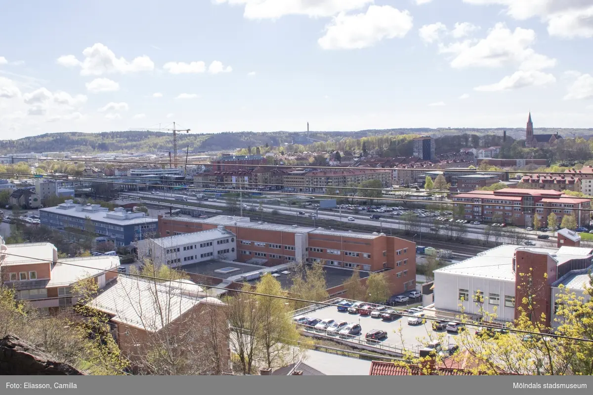 Utsikt från stadsdelen Trädgården i nordost mot Mölndalsbro i sydväst. Vägen strax nedanför är Torggatan. I mitten ligger det röda tegelhuset som är både Polishus och Passexpedition. Mittemot ligger bostadsområdet Timmermannen på Torggatan 64. I fonden ser man Mölndals stad breda ut sig över de tidigare ängsmarkerna. Byggkranen står placerad mitt i SCAs nya kontorsbyggnad vid Mölndals bro. Riskullaverkets skorsten syns långt bort, mitt i bild och Fässbergs kyrka tronar på sin höjd.