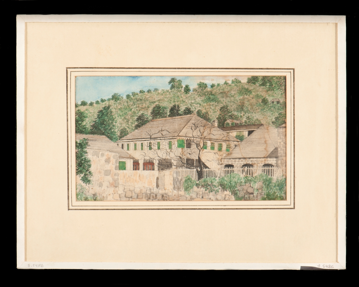 "Guvernementshuset" i Gustavia på Saint Barthelemy. Vitt stenhus under grått tak samt gröna fönsterluckor och omgivet av murar och staket. I bakgrunden skog.