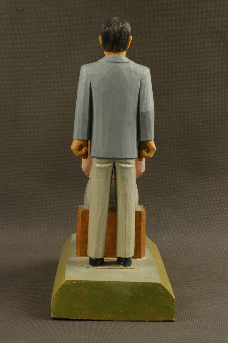 Skåret og delvis malt trefigur på sokkel. Figuren består av en mann og en kvinne. Begge personfigurene er løst nedfelt i sokkelen.