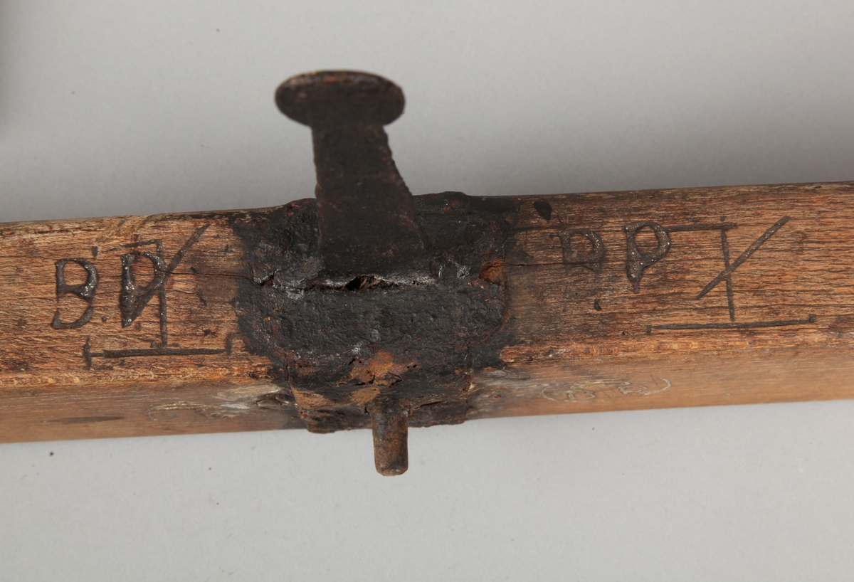 Smal, rektangulær vektarm som smalner i hver ende hvor det er et beslag med en krok hengende. På midten er det et beslag med en gjennomgående bolt til å feste vektarmen i en holder som festes i tak. Der treverket smalner mot endene er det skåret inn tverrgående dekorstriper og på begge sider er det slått inn et rundt merke bestående av små streker. På hver side av treverket ved det midterste beslaget er det slått inn to av disse runde merkene, ett på hver side av metallet. Oppå treverket, på hver side av det midterste beslaget, er det bumerker. På den ene siden av treverket, ved den gjennomgående bolten, er det slått inn to runde merker med bokstavene B.F. med en krone over inni rundingen.