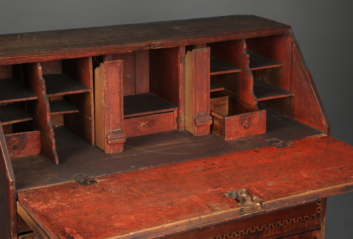 Lyst, rektangulært "slangebuktende" båndt med mørke felter i en bord langs tre sider av skriveplatens front og langs alle sidene av de tre store skuffene og den smale store skuffen.