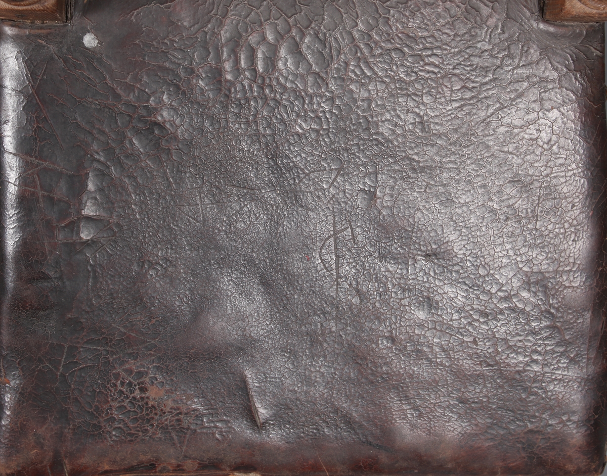 Stol med sete og rygg av lær og med dreiete buete bein. Mellom bein i front er det et utskåret stykke. Rosettformete nagler.